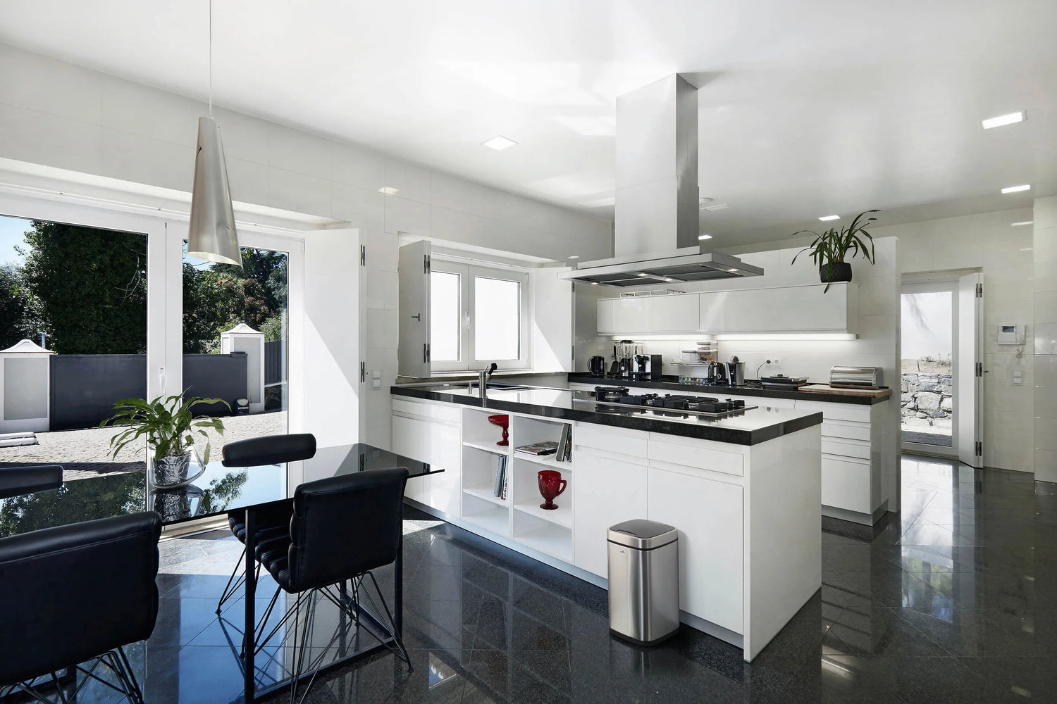 Modern white kitchen with black countertops, stainless steel appliances, and sleek black dining chairs