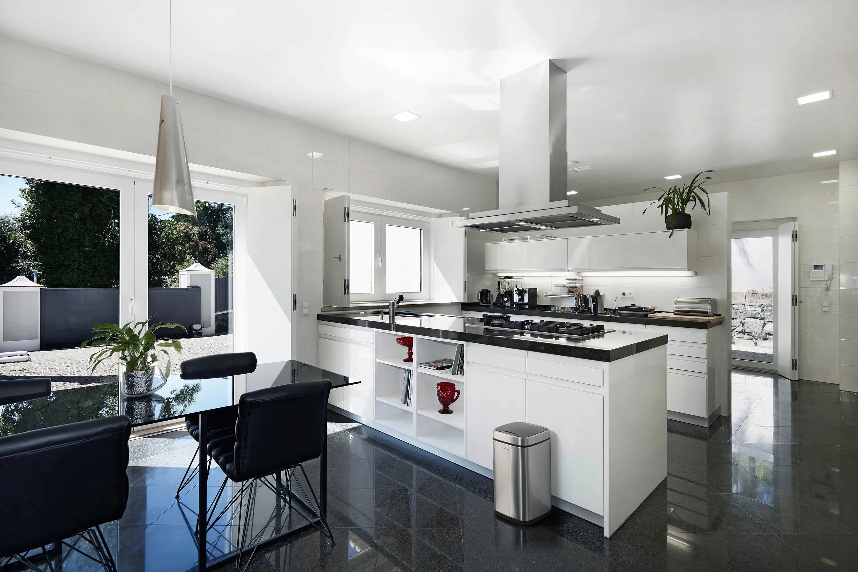 Modern white kitchen with black countertops, stainless steel appliances, and sleek black dining chairs