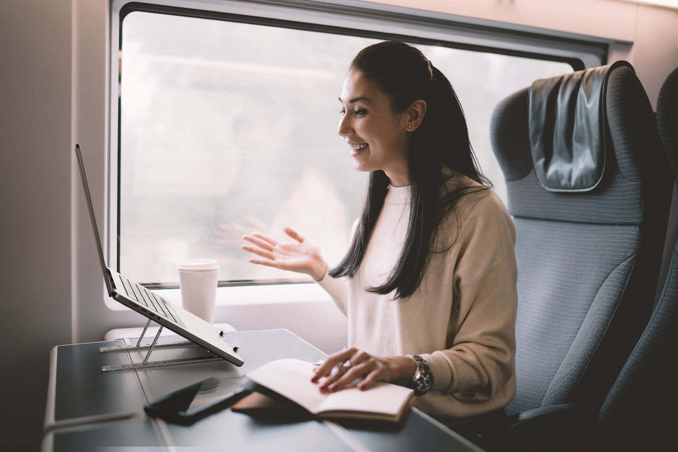 Woman working on laptop during train commute, notebook and coffee on table, ideal for mobile productivity