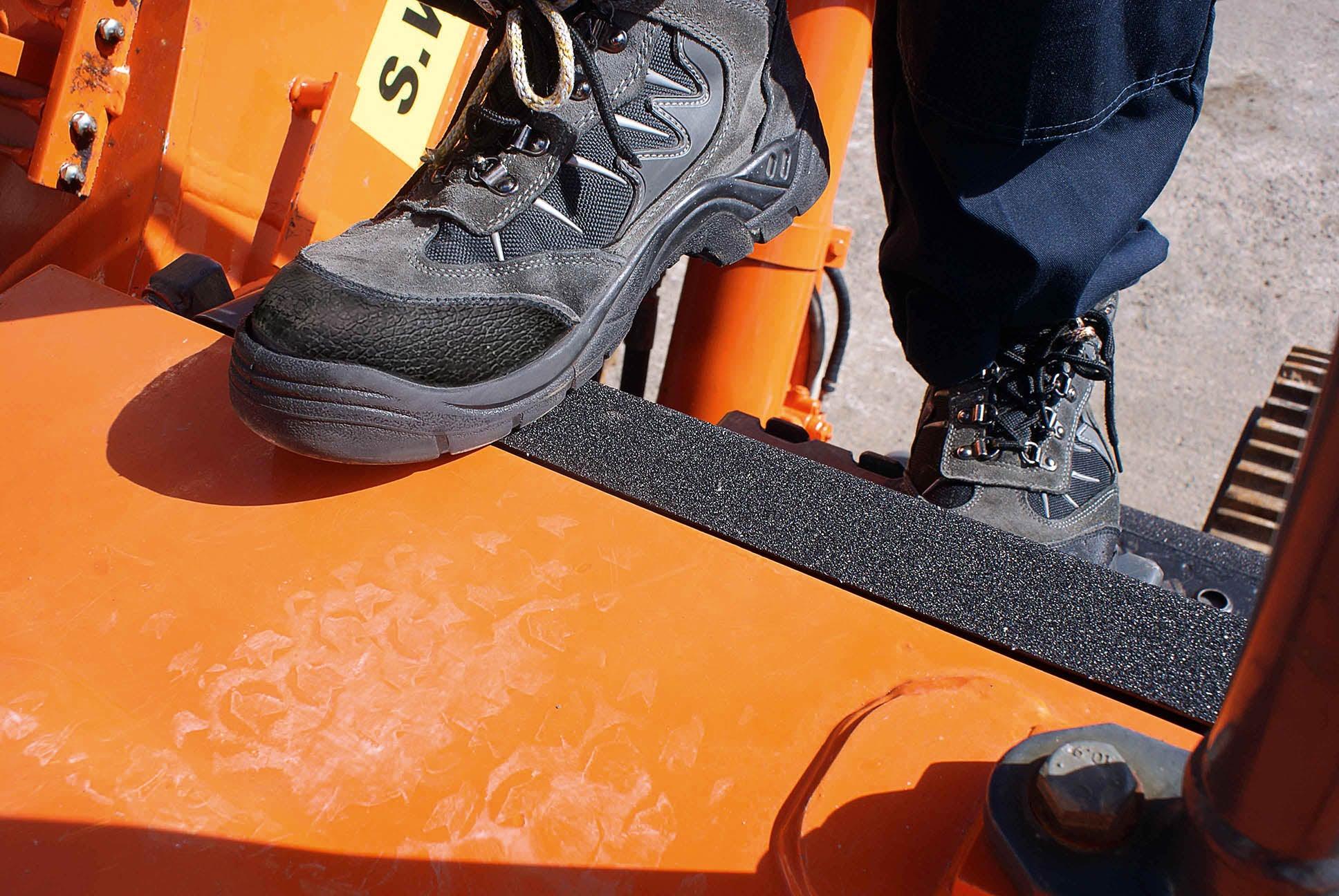 Black safety work boots on orange industrial equipment step with anti-slip tread
