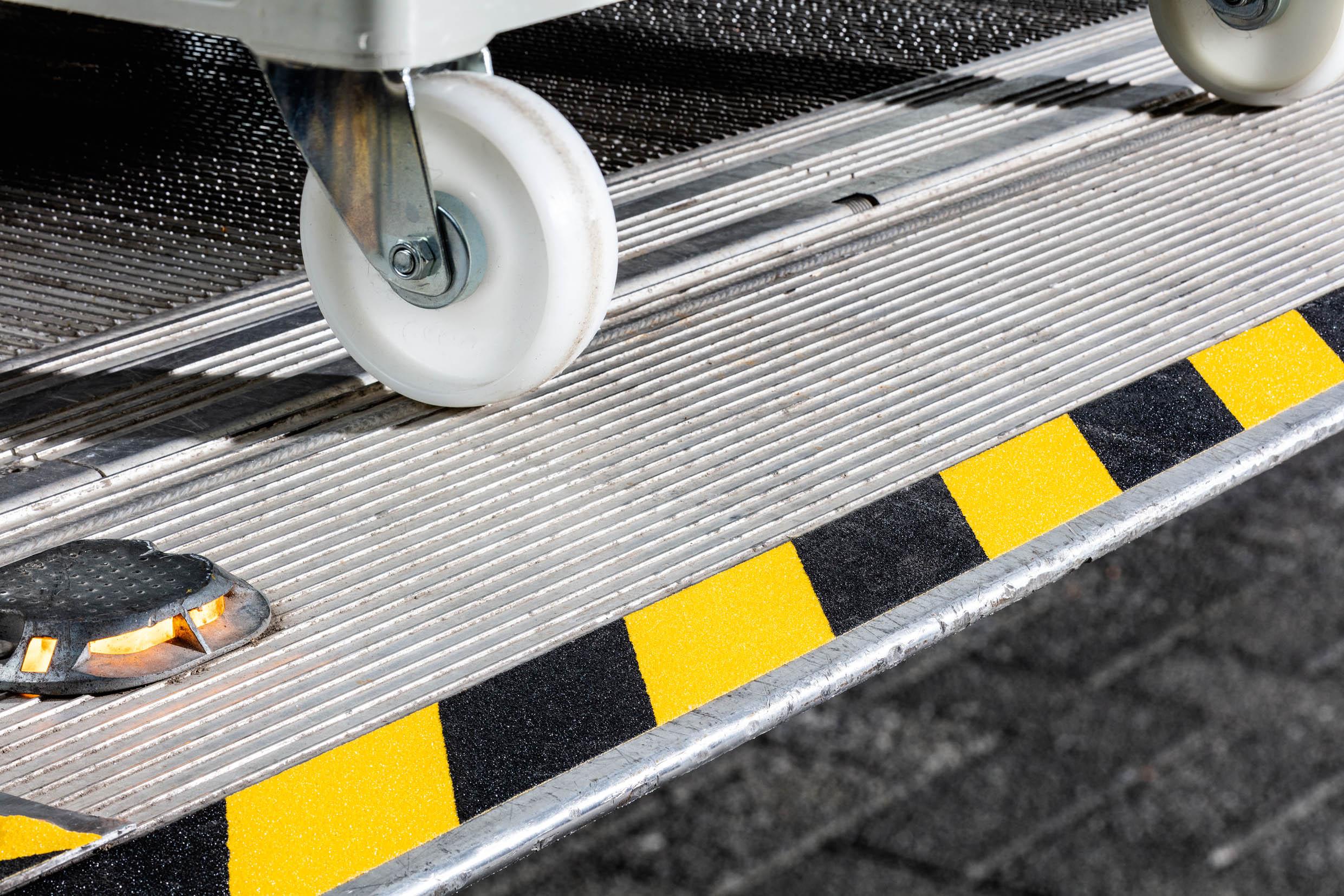 Metal step with yellow black safety stripes and white caster wheel on textured surface