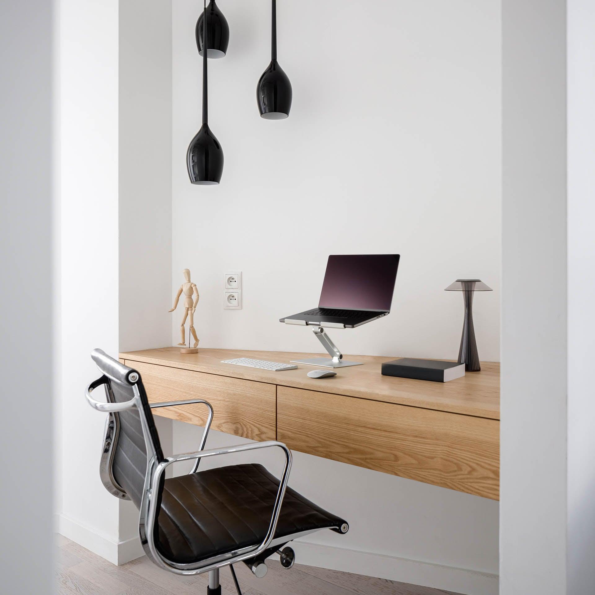 Modern home office desk setup with laptop stand, ergonomic chair, and sleek pendant lights