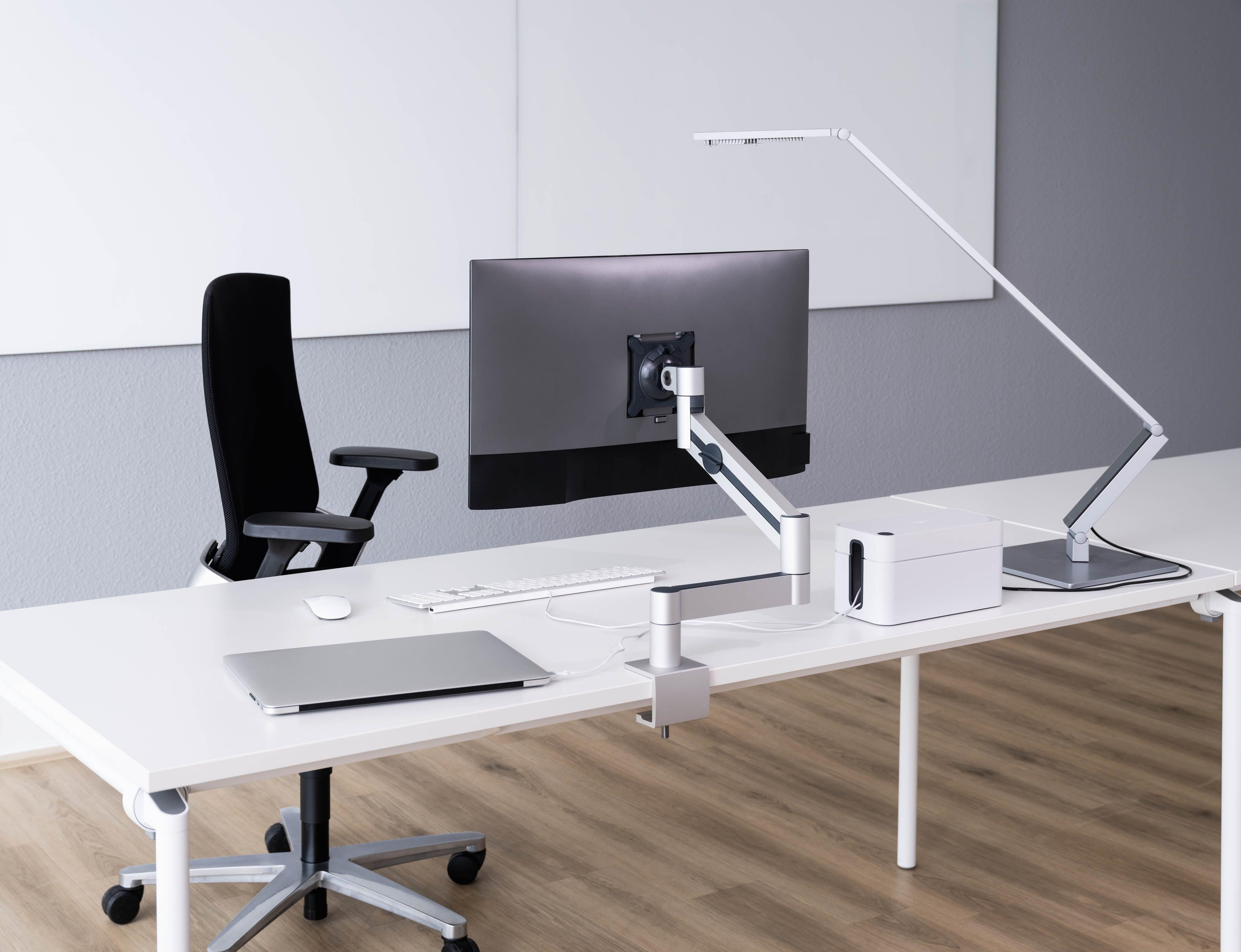 Modern office desk setup with monitor arm, LED lamp, laptop, keyboard, and ergonomic chair