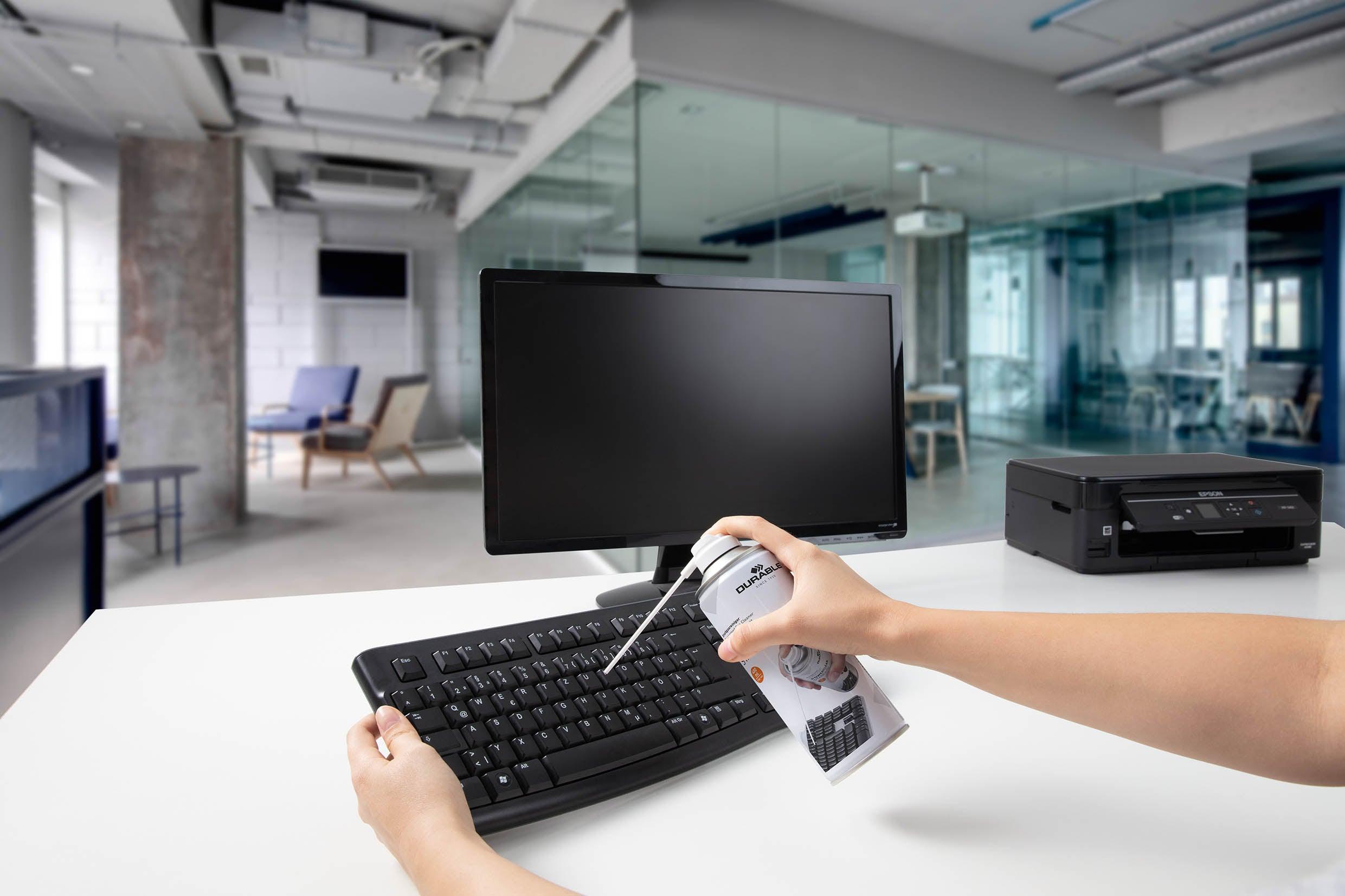 Cleaning office keyboard with compressed air duster in modern workspace
