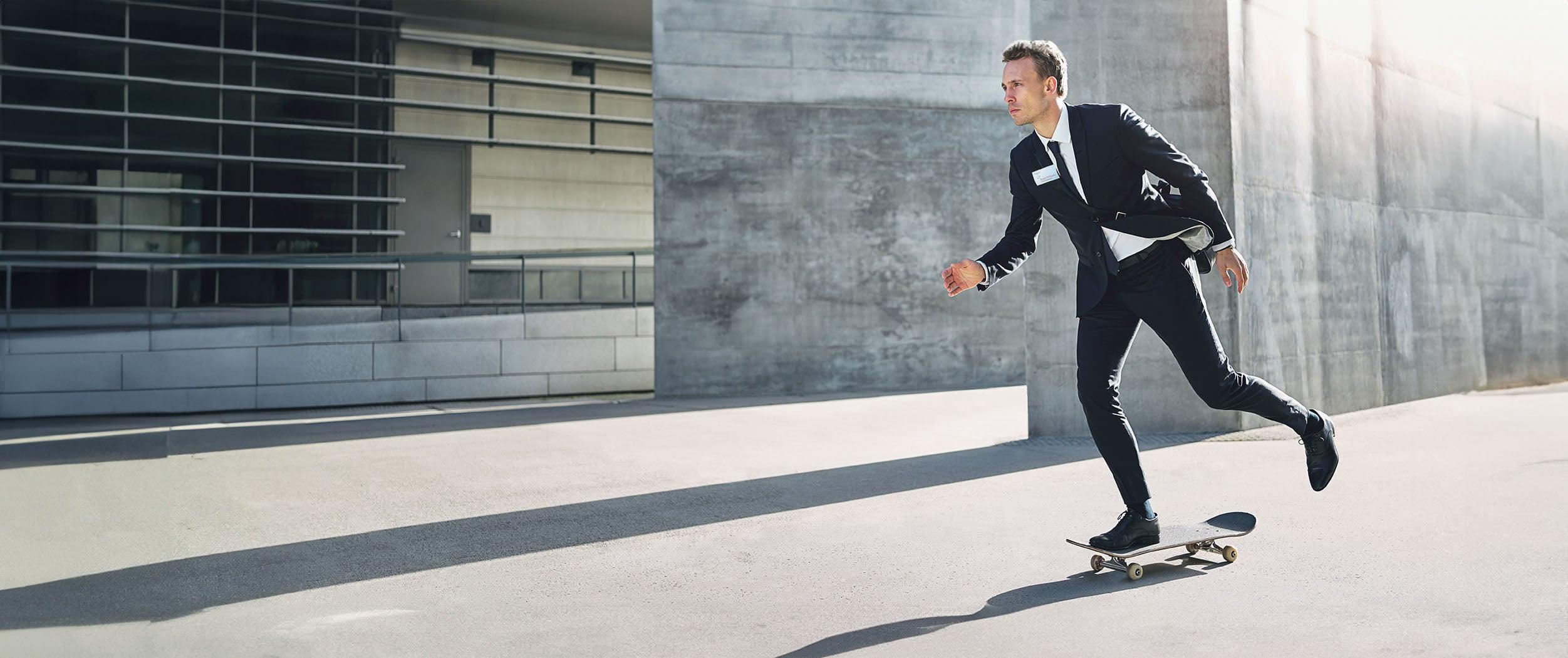 Businessman in suit riding skateboard outside modern office building