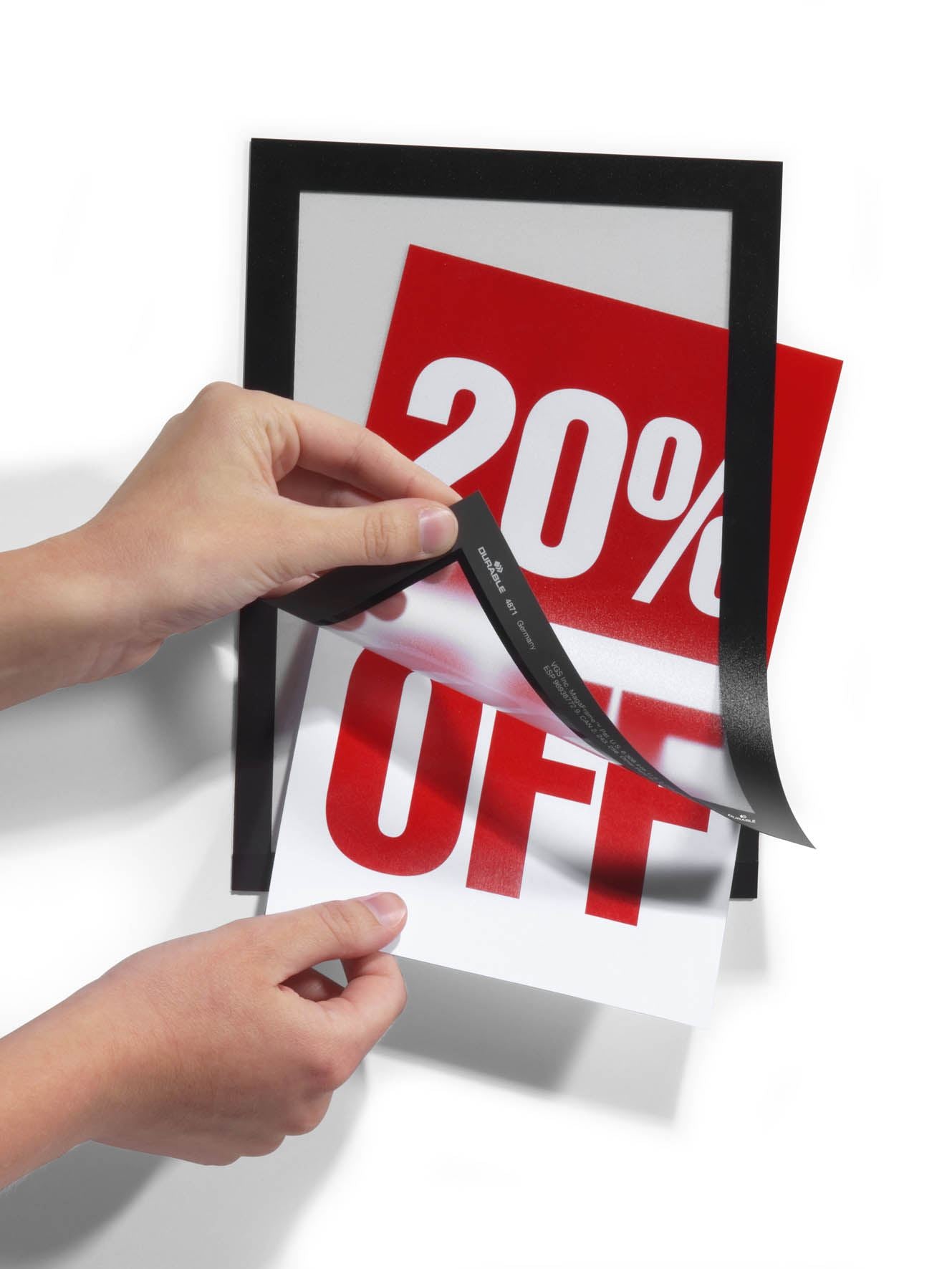 Hands applying black adhesive border to 20% OFF sale sign for retail display